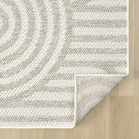 Cream and beige flatweave runner rug with subtle geometric circular and linear pattern, folded corner on light wood floor.