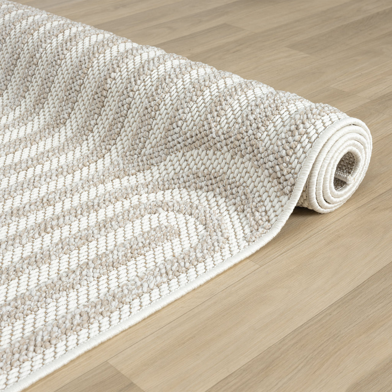 Cream and beige flatweave rug with subtle geometric arch pattern rolled on light wood floor.