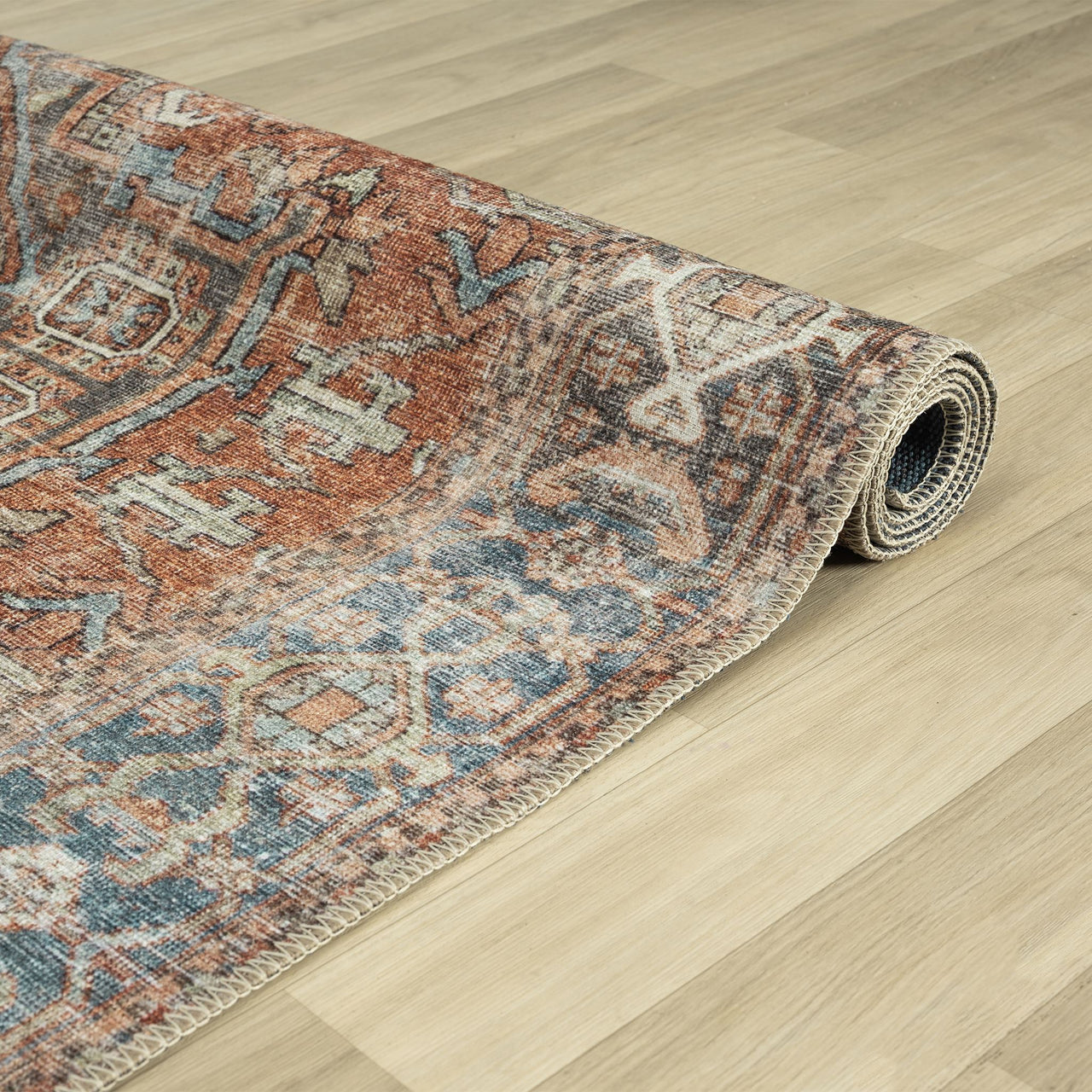 Rolled traditional runner rug with distressed floral patterns in muted blues, rusty reds, and beige tones on a flatweave.