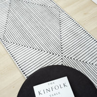 Black and white geometric patterned runner rug with layered linear design on light wood floor.