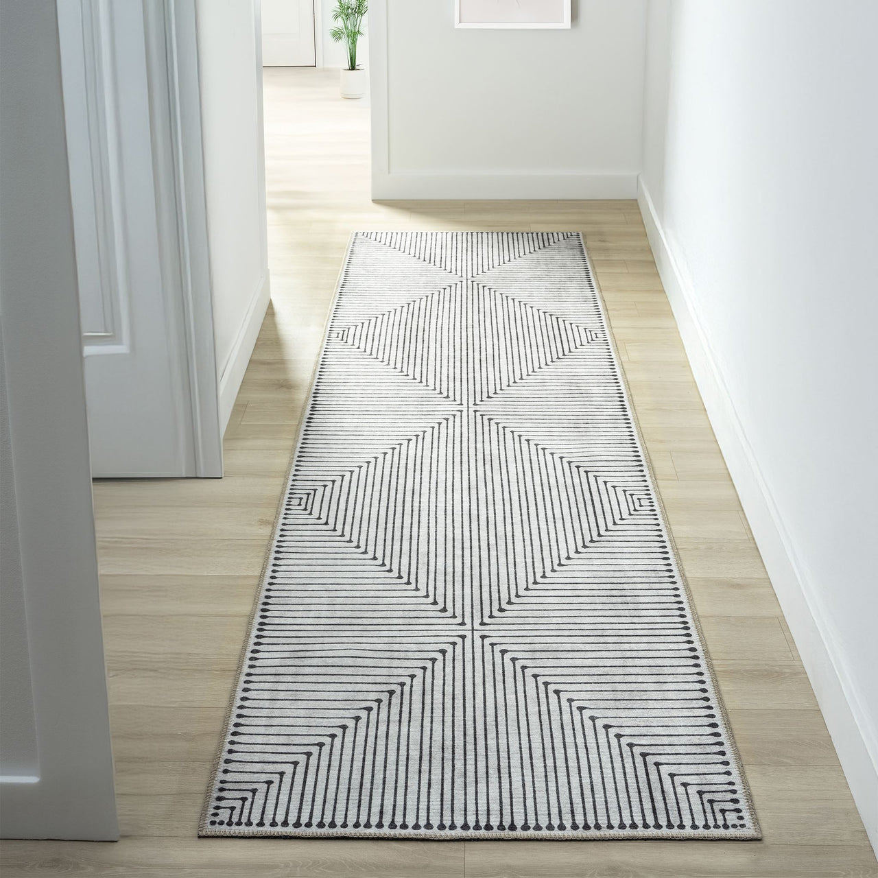 Long narrow runner rug with black and white geometric striped triangles and a thin black border on a light wood floor hallway.
