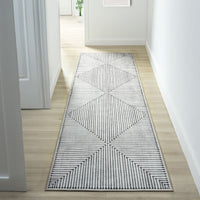 Long narrow runner rug with black and white geometric striped triangles and a thin black border on a light wood floor hallway.