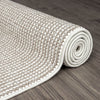 Beige flatweave rug with textured geometric pattern rolled on dark hardwood floor.