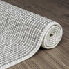 Rolled grey and white flatweave rug with a textured geometric pattern on wooden floor.