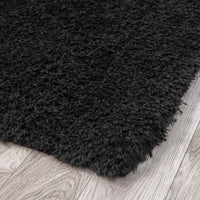 Black modern shaggy rug with thick plush polyester fibers on light wood floor.
