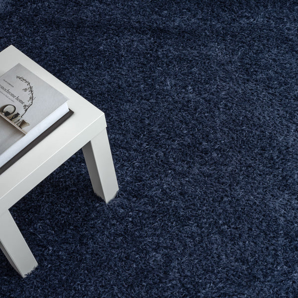 Navy blue modern shaggy rug with dense polyester pile under white table corner.