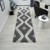 Grey and white geometric patterned runner rug with fringed edges on light wood floor.