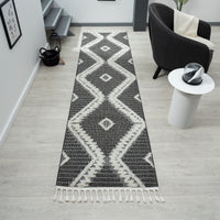 Grey and white geometric patterned runner rug with fringed edges on light wood floor.