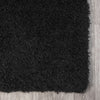 Black modern shaggy rug with dense plush polyester fibers on light wood floor.
