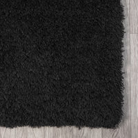 Black modern shaggy rug with dense plush polyester fibers on light wood floor.
