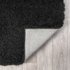 Black modern shaggy rug with thick polyester fibers and non-slip backing on light wood floor.