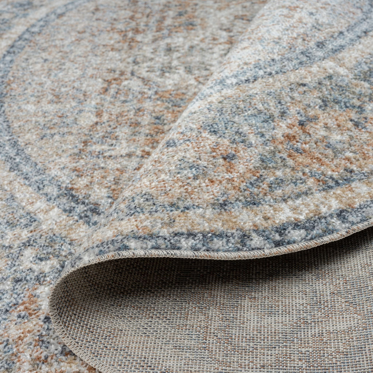 Round coral rug with layered circular patterns in soft blue and beige tones, textured polyester weave.