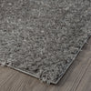 Grey and silver modern shaggy polyester rug corner on wooden floor.