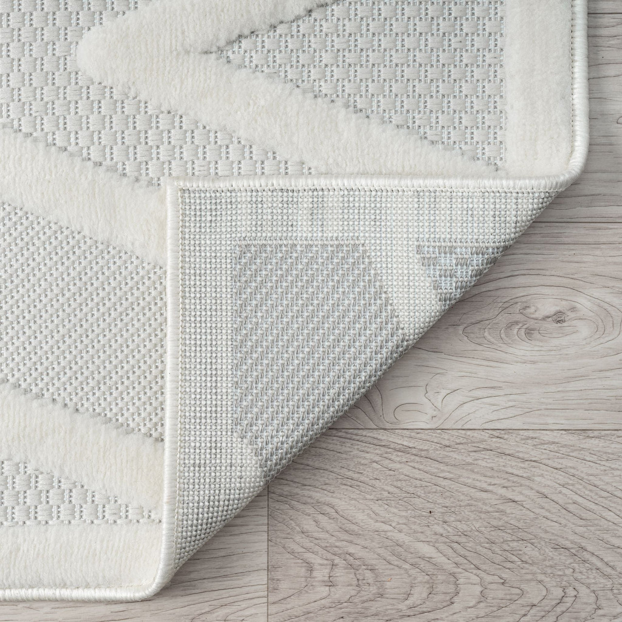 Gray and white runner rug with textured geometric chevron and hexagon patterns, folded corner showing woven backing.