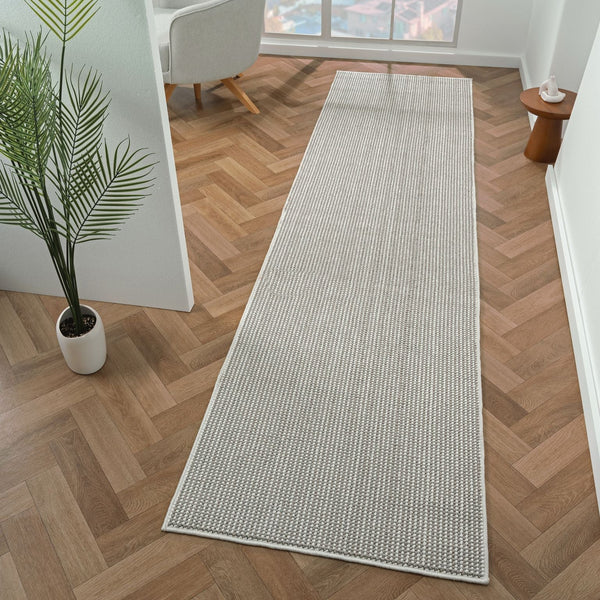 Grey flatweave runner rug with subtle linear geometric pattern on wood parquet floor.
