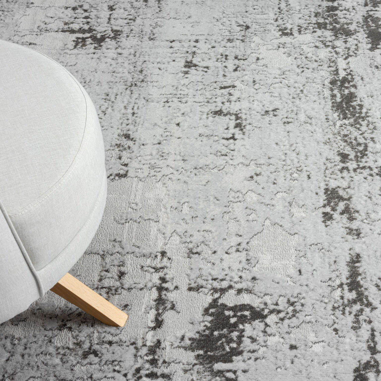 Gray textured rug with a beige chair with wooden base.