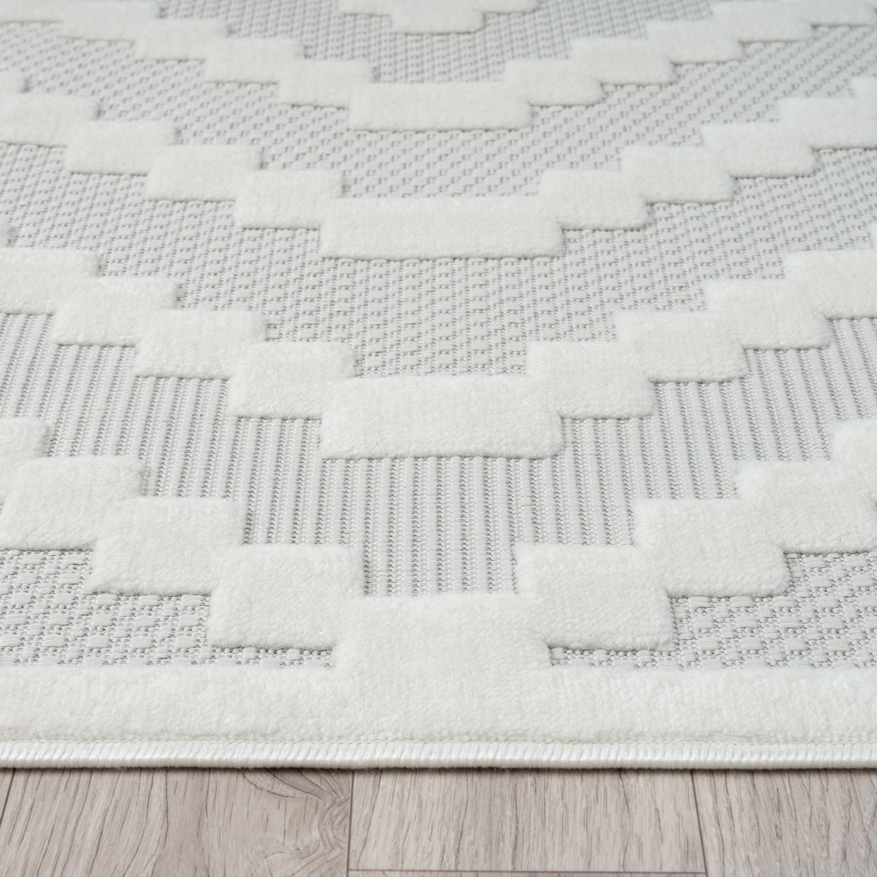 Cream and beige geometric patterned rug with textured polypropylene pile on wood floor.