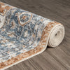 Rolled transitional rug with blue, beige, and gray intricate floral pattern on hardwood floor.