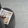 Grey flatweave rug with subtle textured pattern under dark grey ottoman and open magazine.