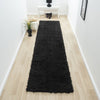 Black modern shaggy runner rug with dense plush texture on light wood floor in narrow hallway.