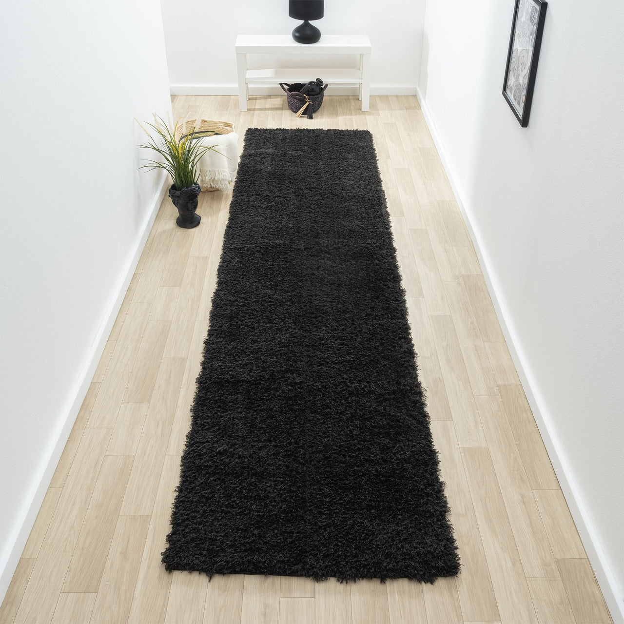 Black modern shaggy runner rug with dense plush texture on light wood floor in narrow hallway.