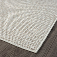 Beige flatweave rug with a subtle textured geometric pattern and clean edge on dark hardwood floor.