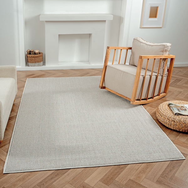 Grey flatweave rug with subtle textured geometric pattern on wood herringbone floor.