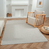 Grey flatweave rug with subtle textured geometric pattern on wood herringbone floor.
