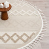 Beige round rug with cream geometric diamond patterns and fringe border on light wood floor.