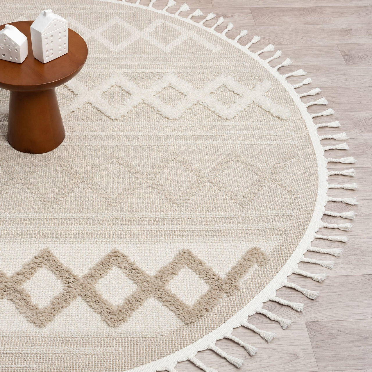 Beige round rug with cream geometric diamond patterns and fringe border on light wood floor.