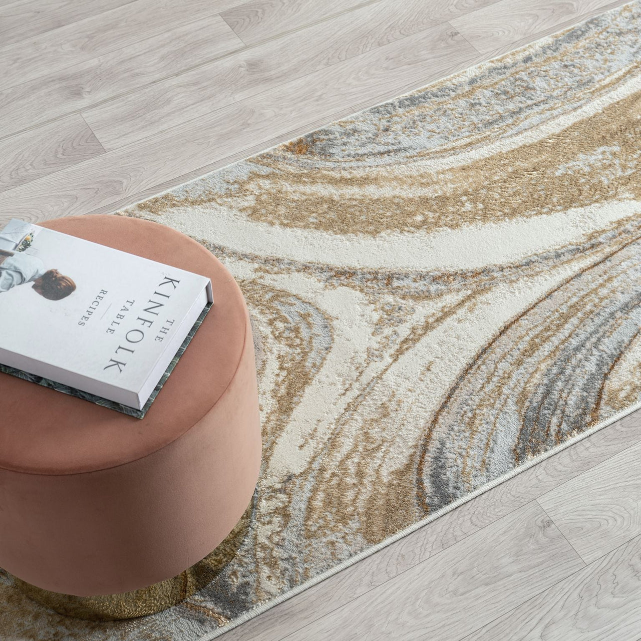 Decorative rug with abstract pattern on a wooden floor next to a pink stool and book.