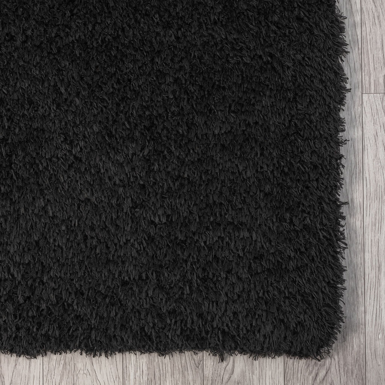 Black modern shaggy runner rug with thick plush polyester pile on light wood floor.