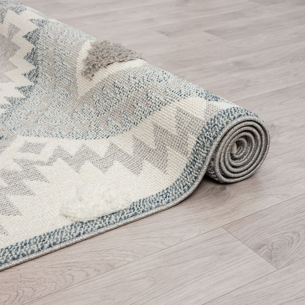 Rolled grey and cream runner rug with textured geometric zigzag and dotted patterns, fringed ends.