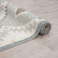 Rolled grey and cream runner rug with textured geometric zigzag and dotted patterns, fringed ends.