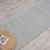 Soft grey shaggy runner rug on light wood floor with woven basket side table.