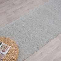Soft grey shaggy runner rug on light wood floor with woven basket side table.