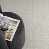 Beige flatweave rug with subtle geometric pattern under dark gray upholstered furniture with an open book.