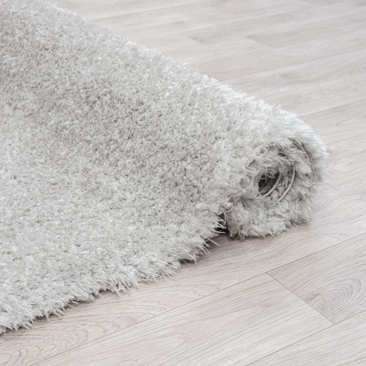 Rolled grey shaggy rug with soft, dense polyester fibers on light wood floor.