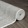 Rolled silver grey flatweave rug with textured geometric pattern on dark wood floor.