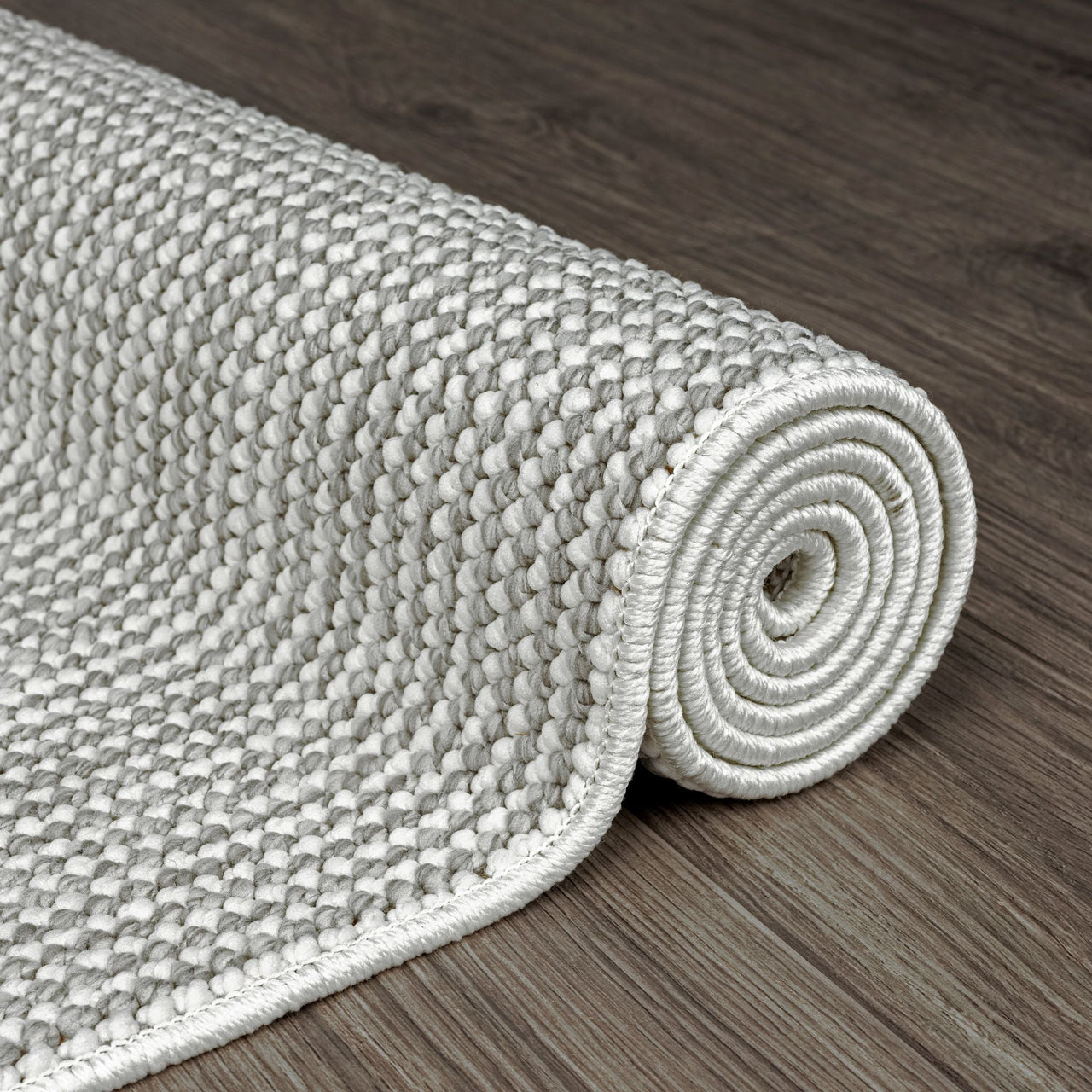 Rolled silver grey flatweave rug with textured geometric pattern on dark wood floor.
