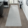 Grey flatweave runner rug with subtle geometric pattern on wood floor in bright hallway.