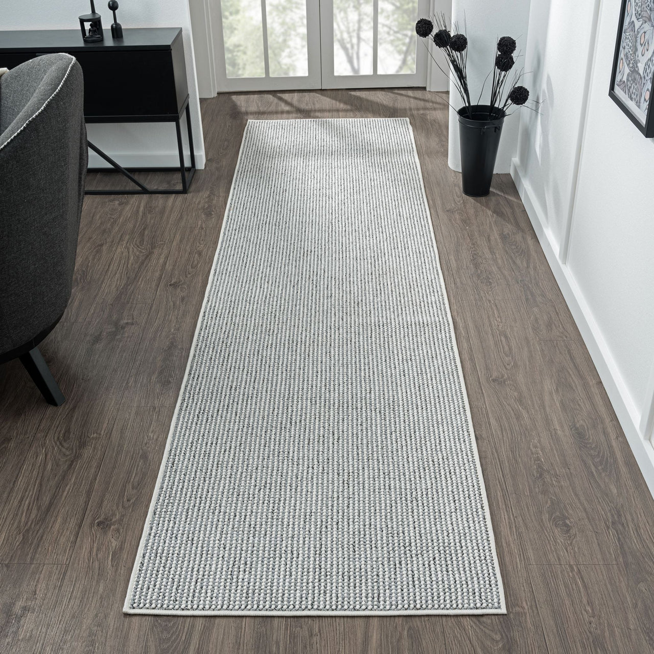 Grey flatweave runner rug with subtle geometric pattern on wood floor in bright hallway.