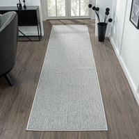 Grey flatweave runner rug with subtle geometric pattern on wood floor in bright hallway.
