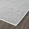 Grey flatweave rug with a subtle textured geometric pattern and white border on wood floor.