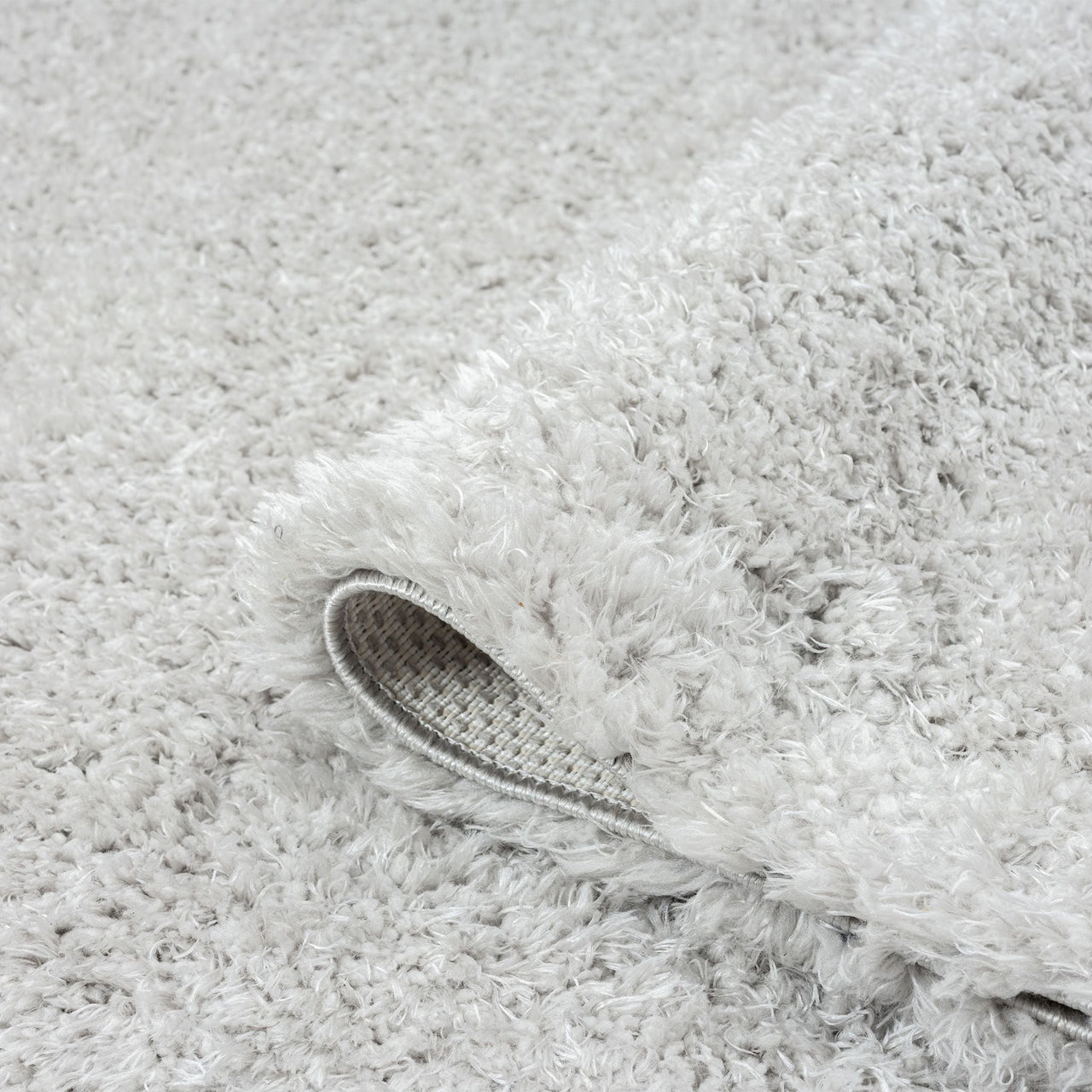 Soft grey shaggy runner rug with thick plush pile and textured backing visible on curled edge.