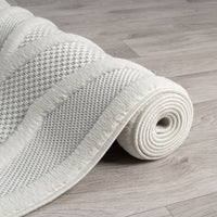 Cream geometric patterned rug with textured polypropylene pile, softly rolled on light wood floor.
