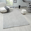 Light grey modern shaggy rug on light wood floor with round white chair and ottoman nearby.