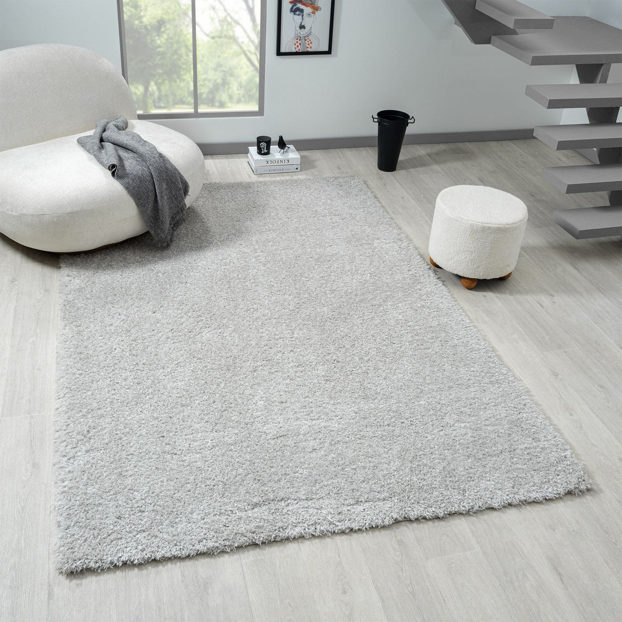 Light grey modern shaggy rug on light wood floor with round white chair and ottoman nearby.