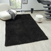 Black modern shaggy rug with dense polyester pile on light wood floor in contemporary living room setting.