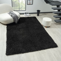 Black modern shaggy rug with dense polyester pile on light wood floor in contemporary living room setting.